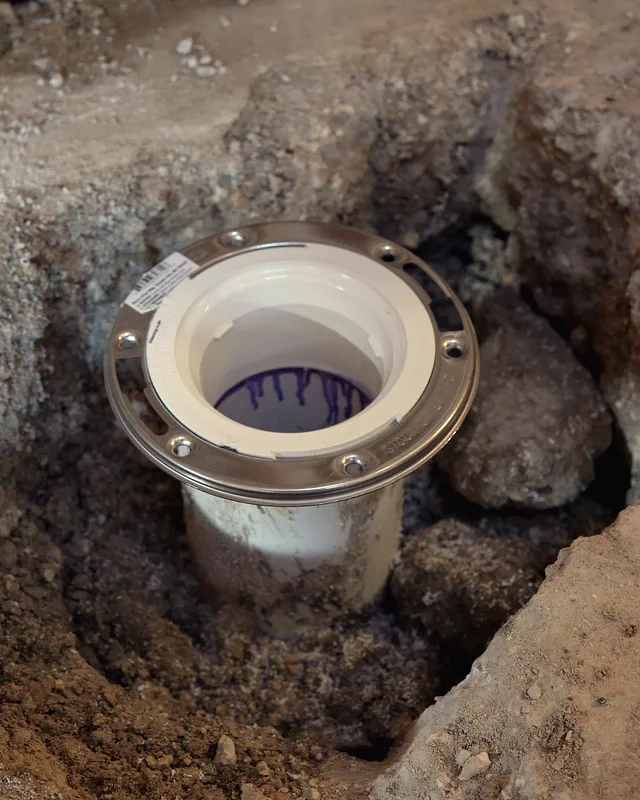 A new white PVC drain with a stainless ring, set in a trench cut through a concrete slab.
