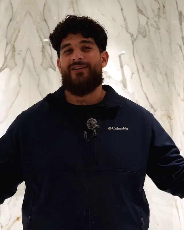 The owner of H&S Plumbing in a navy jacket, standing in a white marble walk-in shower.