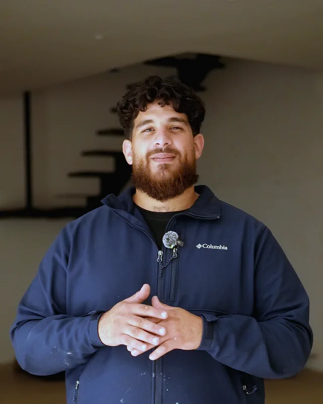 The owner of H&S Plumbing in a navy jacket, hands together, in the living room of a new Houston home.