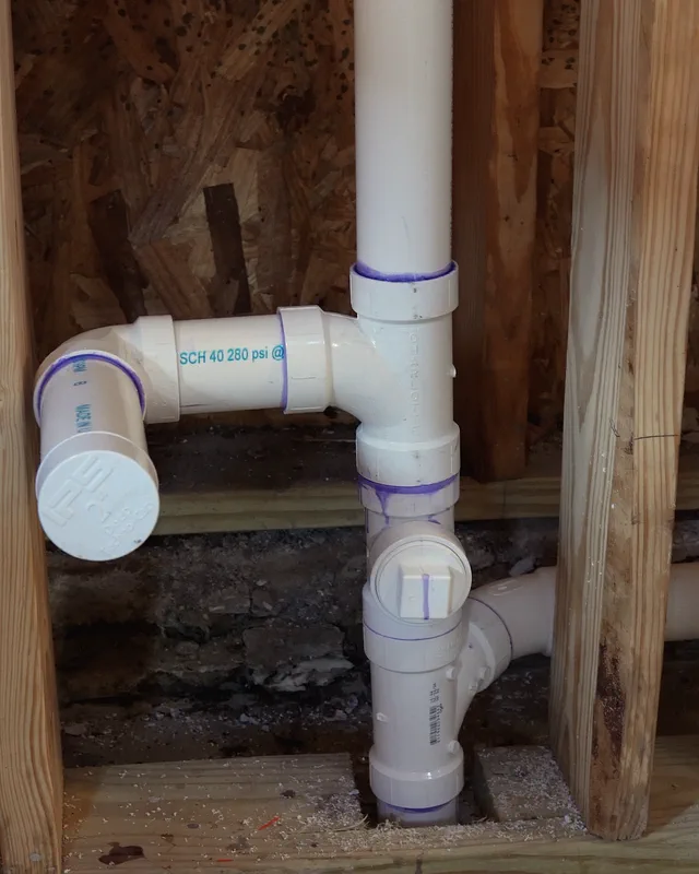 New white PVC drain piping in an open stud wall: a stack with a cleanout and a capped branch.